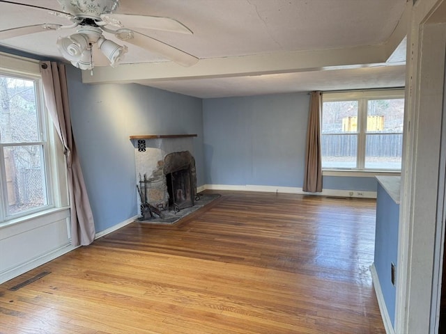 unfurnished living room with visible vents, baseboards, ceiling fan, a fireplace, and light wood finished floors