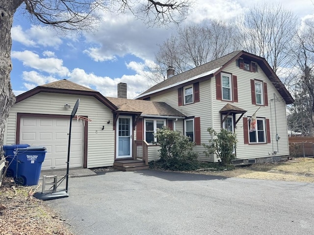 view of front of house featuring aphalt driveway, a shingled roof, a garage, and a chimney