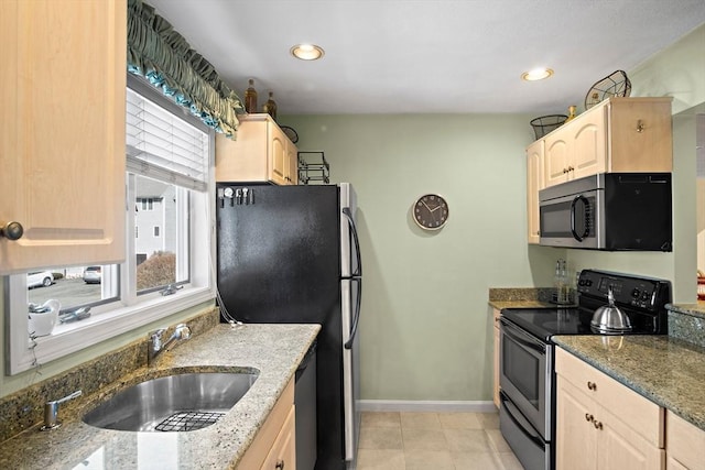 kitchen featuring stone countertops, stainless steel appliances, a sink, baseboards, and light brown cabinetry