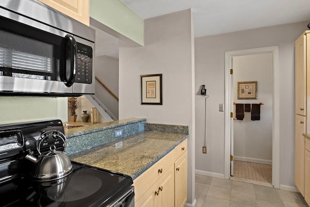 kitchen with light tile patterned floors, stone counters, baseboards, range, and stainless steel microwave