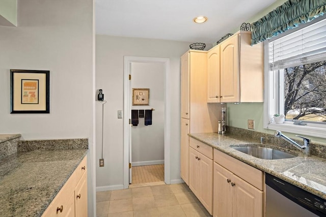 kitchen featuring light brown cabinetry, a sink, light stone countertops, dishwasher, and baseboards