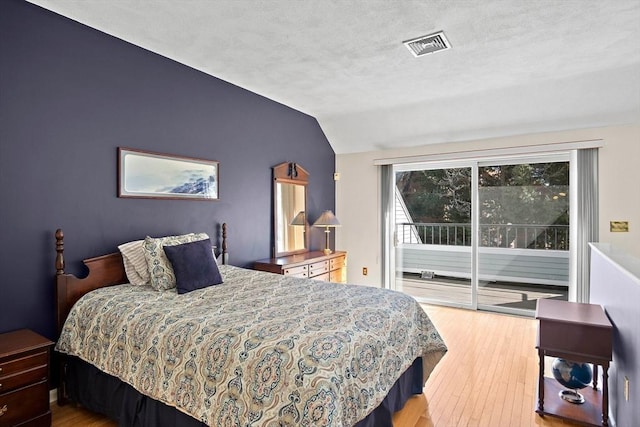 bedroom featuring lofted ceiling, a textured ceiling, wood finished floors, visible vents, and access to outside