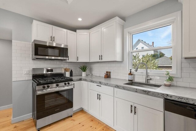 kitchen with decorative backsplash, appliances with stainless steel finishes, a sink, white cabinets, and light wood finished floors