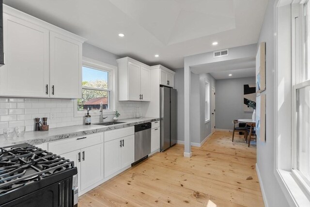 kitchen with backsplash, visible vents, appliances with stainless steel finishes, light wood-type flooring, and a sink