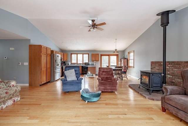 living room with a wood stove, ceiling fan, lofted ceiling, and light wood-type flooring