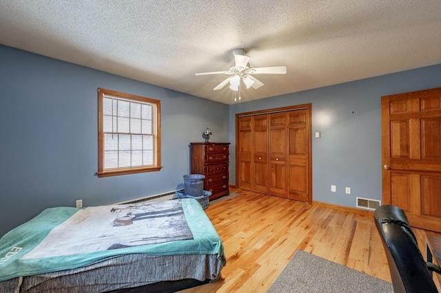 bedroom featuring a textured ceiling, ceiling fan, baseboard heating, light hardwood / wood-style flooring, and a closet