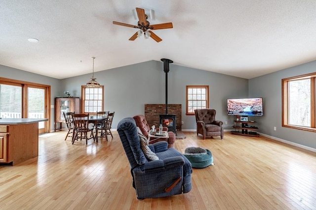 living room featuring ceiling fan, light wood-type flooring, a wood stove, and vaulted ceiling