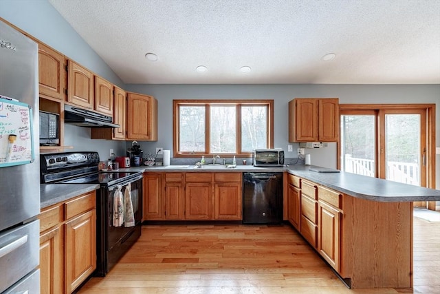 kitchen with kitchen peninsula, light wood-type flooring, vaulted ceiling, sink, and black appliances