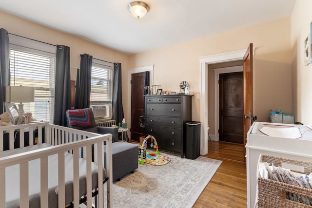 bedroom featuring cooling unit, light wood-type flooring, and a nursery area