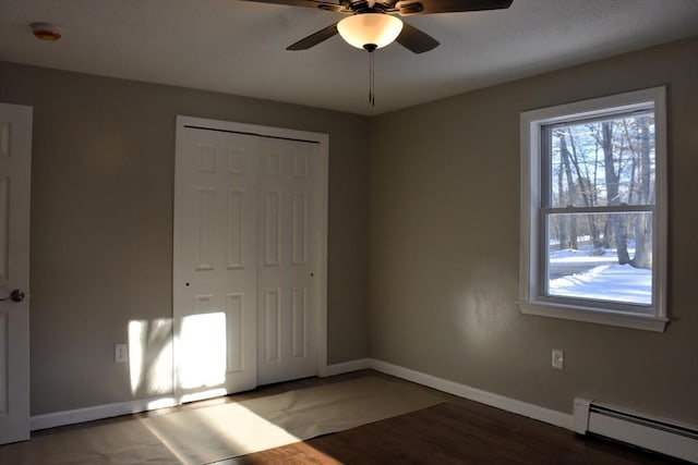 unfurnished bedroom with ceiling fan, a baseboard heating unit, wood finished floors, baseboards, and a closet