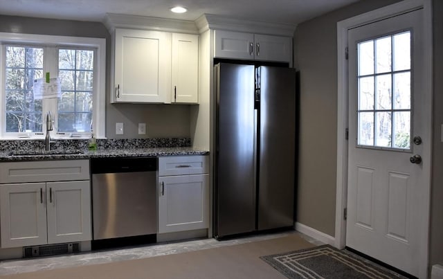 kitchen with baseboards, white cabinets, dark stone counters, appliances with stainless steel finishes, and a sink