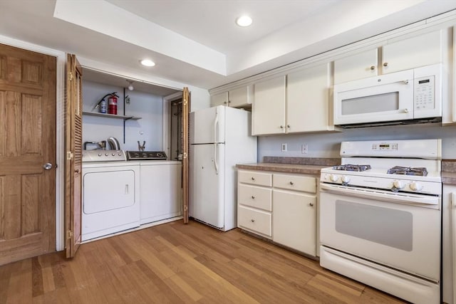 kitchen featuring white appliances, white cabinetry, light hardwood / wood-style floors, washer and dryer, and a raised ceiling