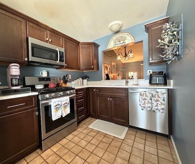 kitchen with light tile patterned flooring, sink, dark brown cabinets, pendant lighting, and stainless steel appliances