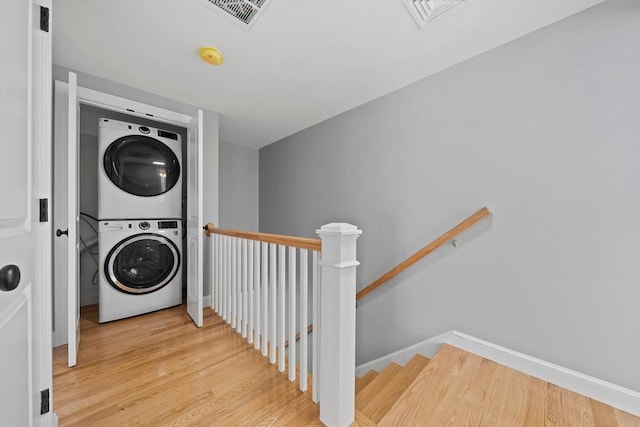 laundry room with light hardwood / wood-style flooring and stacked washing maching and dryer