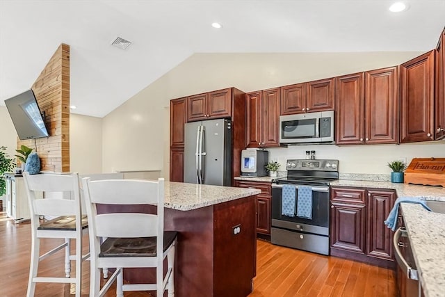 kitchen featuring visible vents, appliances with stainless steel finishes, a breakfast bar area, vaulted ceiling, and light wood-type flooring