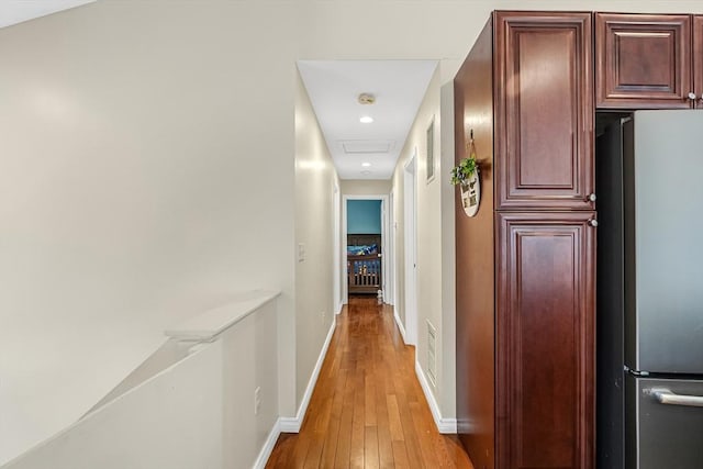 hallway with attic access, visible vents, light wood-style flooring, and baseboards