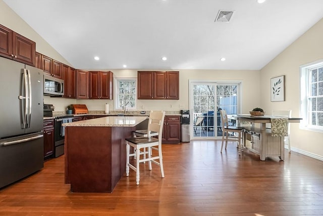 kitchen featuring visible vents, lofted ceiling, a breakfast bar area, appliances with stainless steel finishes, and dark wood-style flooring