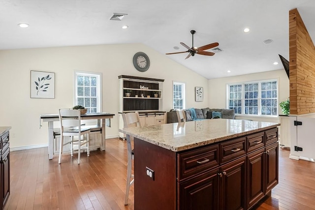 kitchen featuring visible vents, dark wood finished floors, a breakfast bar area, light stone countertops, and vaulted ceiling