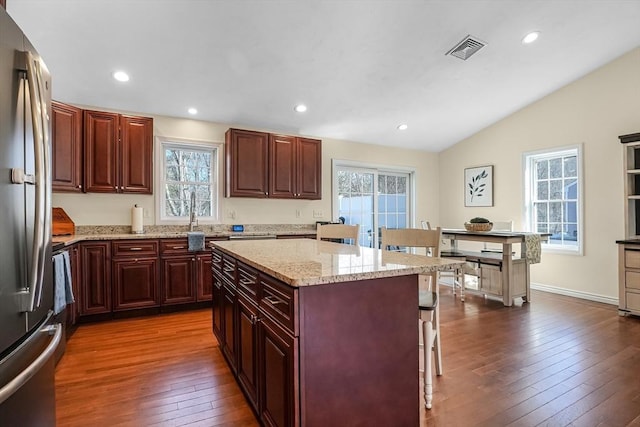 kitchen featuring a breakfast bar, a kitchen island, visible vents, stainless steel fridge, and dark wood finished floors