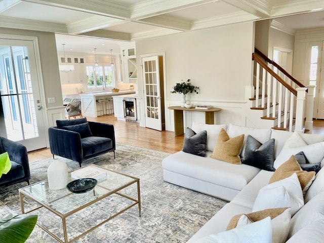 living room featuring coffered ceiling, crown molding, beverage cooler, and light hardwood / wood-style floors