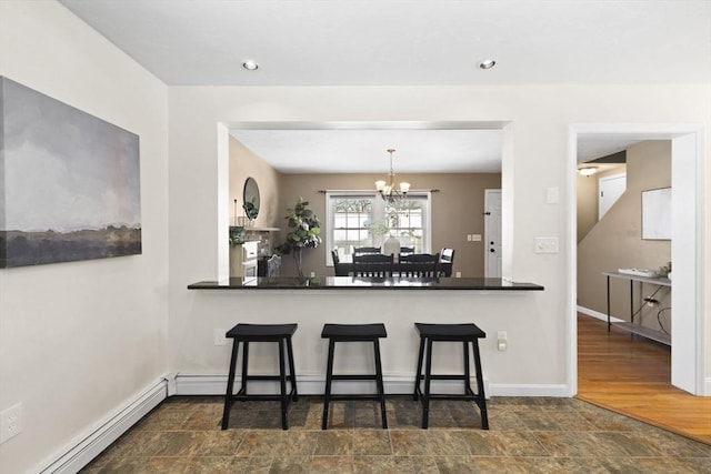 kitchen with a kitchen bar, a baseboard radiator, kitchen peninsula, and an inviting chandelier