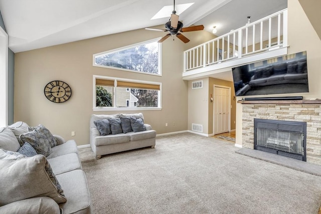 carpeted living room with a stone fireplace, ceiling fan, and lofted ceiling with skylight