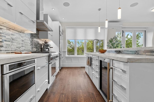 kitchen with modern cabinets, premium appliances, a wall mounted air conditioner, wall chimney range hood, and white cabinetry
