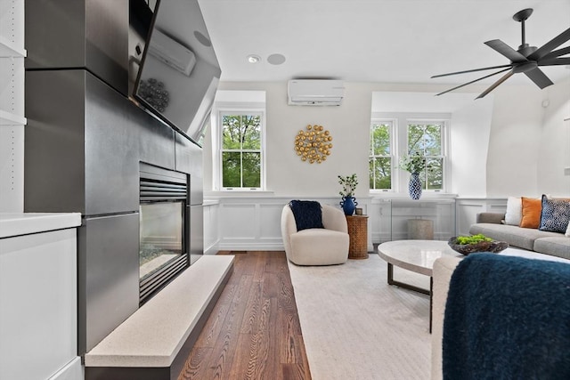 living area with dark wood-type flooring, a wall mounted air conditioner, a fireplace, ceiling fan, and wainscoting