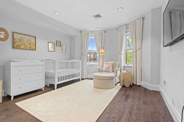 bedroom featuring dark wood finished floors, baseboards, a crib, and recessed lighting
