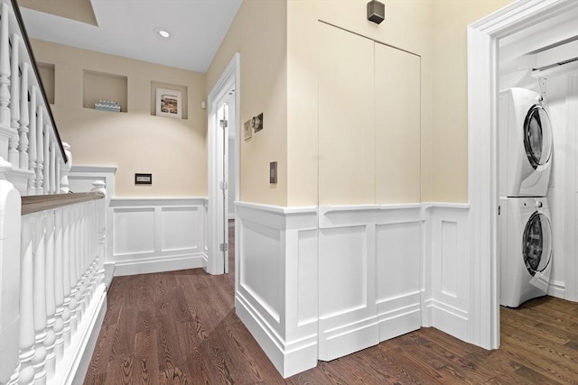 clothes washing area with stacked washer / drying machine, a decorative wall, a wainscoted wall, dark wood-type flooring, and recessed lighting