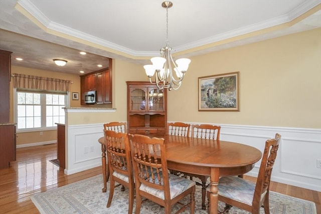 dining room with crown molding, light wood finished floors, a wainscoted wall, and a chandelier