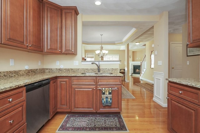 kitchen with a sink, a raised ceiling, stainless steel dishwasher, and light wood-type flooring