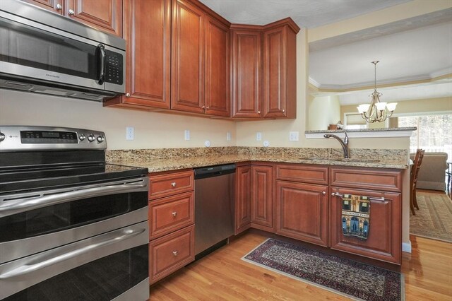 kitchen featuring appliances with stainless steel finishes, a sink, light wood-style floors, a chandelier, and a peninsula