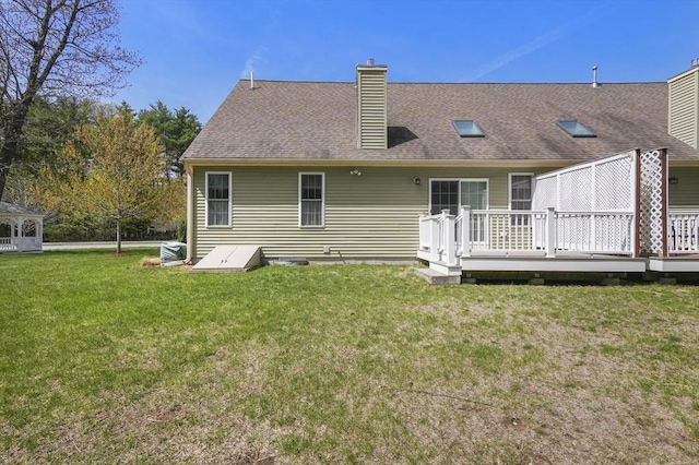 back of house featuring roof with shingles, a chimney, a yard, and a deck