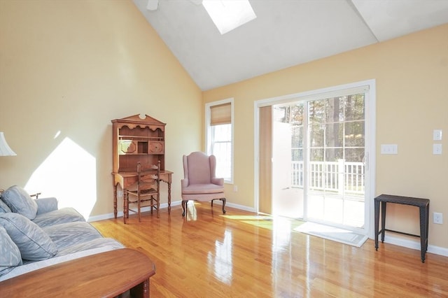 living area with light wood-style floors, baseboards, high vaulted ceiling, and a skylight