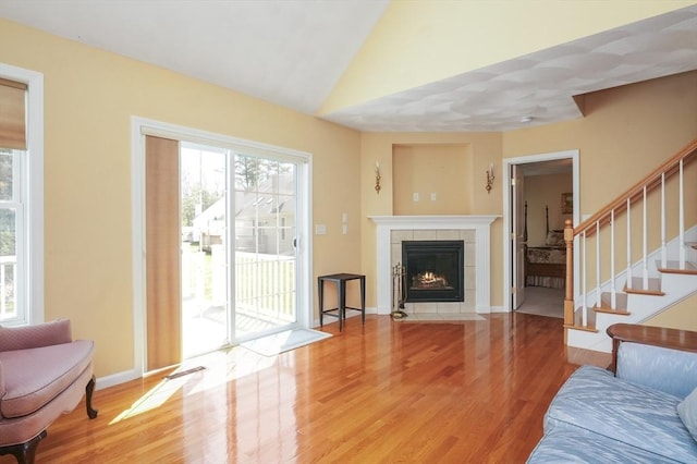 living room with stairway, a tile fireplace, lofted ceiling, and light wood-style floors