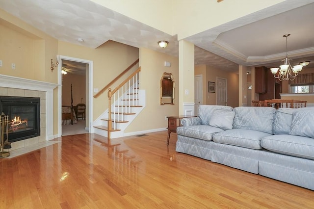 living area with an inviting chandelier, wood finished floors, a fireplace, stairway, and a tray ceiling