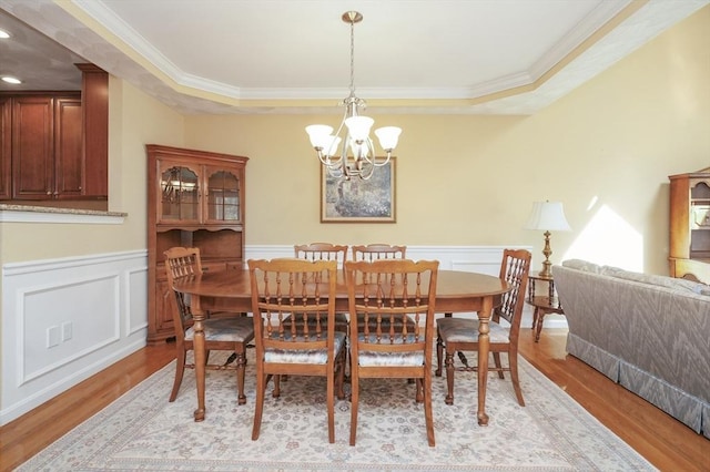 dining area with crown molding, a decorative wall, a wainscoted wall, light wood-style flooring, and a notable chandelier