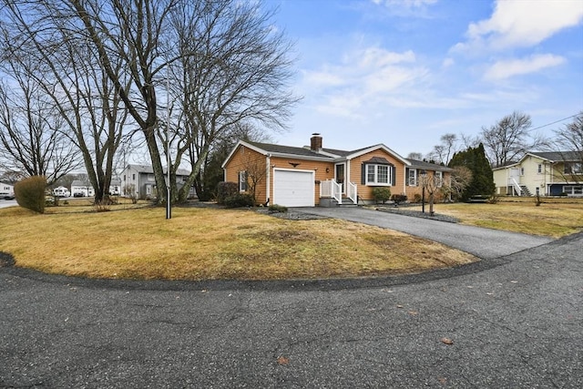 view of front of home with an attached garage, aphalt driveway, a chimney, and a front yard