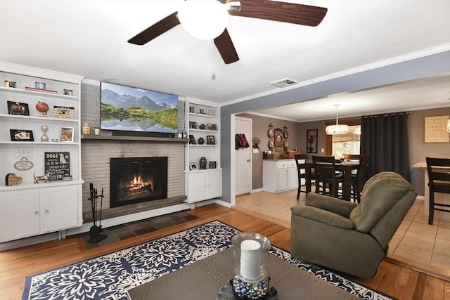 living area with ornamental molding, a brick fireplace, wood finished floors, and visible vents