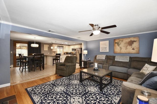 living room with light wood-style flooring, a ceiling fan, baseboards, visible vents, and crown molding