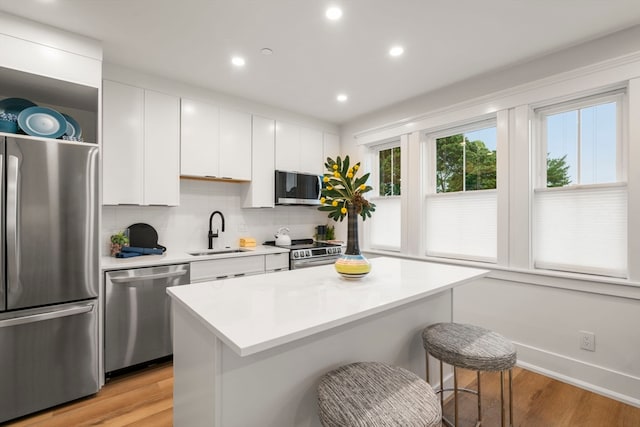 kitchen with a center island, white cabinets, sink, appliances with stainless steel finishes, and light hardwood / wood-style floors