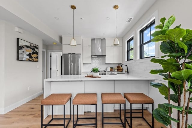 130 Cushing St Unit Ph1, Cambridge, MA 02138 - kitchen with stainless steel fridge, wall chimney range hood, a peninsula, white cabinets, and backsplash