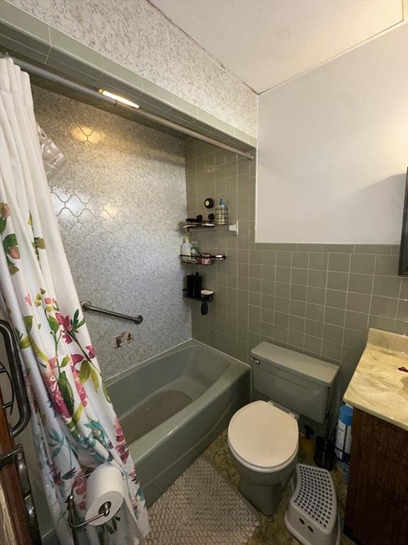 full bathroom featuring vanity, toilet, tile walls, and shower / bath combo with shower curtain