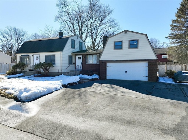 dutch colonial featuring brick siding, a gambrel roof, fence, a garage, and driveway