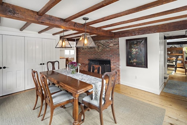 dining area with a fireplace, beam ceiling, and light hardwood / wood-style flooring