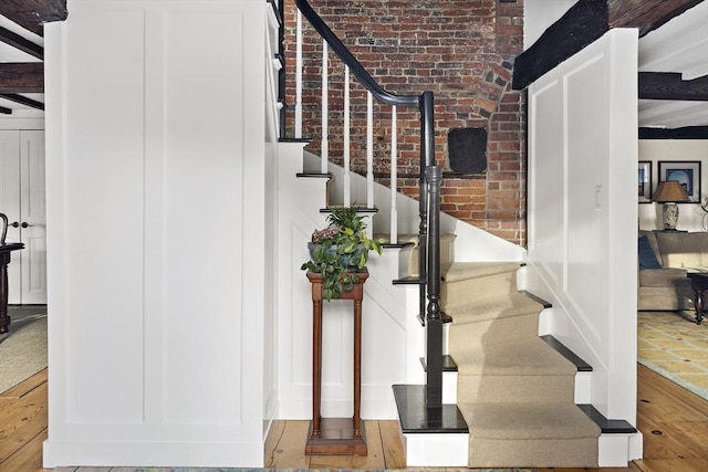 stairs with wood-type flooring and brick wall