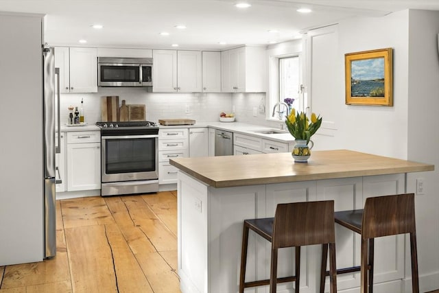 kitchen with a breakfast bar, sink, white cabinetry, kitchen peninsula, and stainless steel appliances