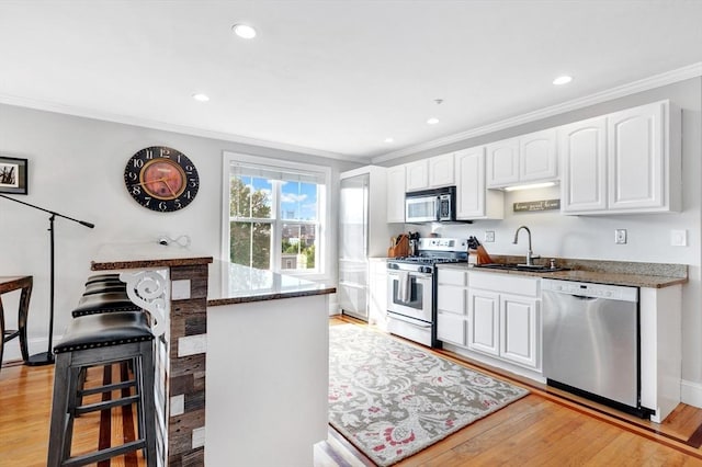 kitchen with a sink, light wood-style floors, white cabinets, crown molding, and appliances with stainless steel finishes