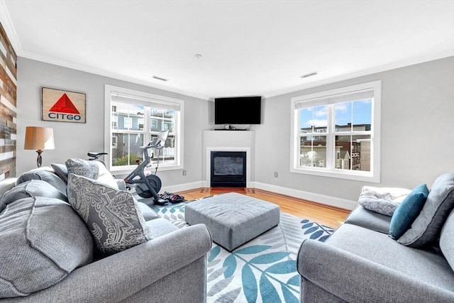 living room with ornamental molding, wood finished floors, a glass covered fireplace, and visible vents